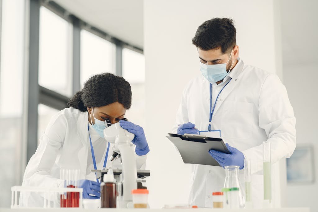 Two scientists working with microscope and clipboard in a lab setting.